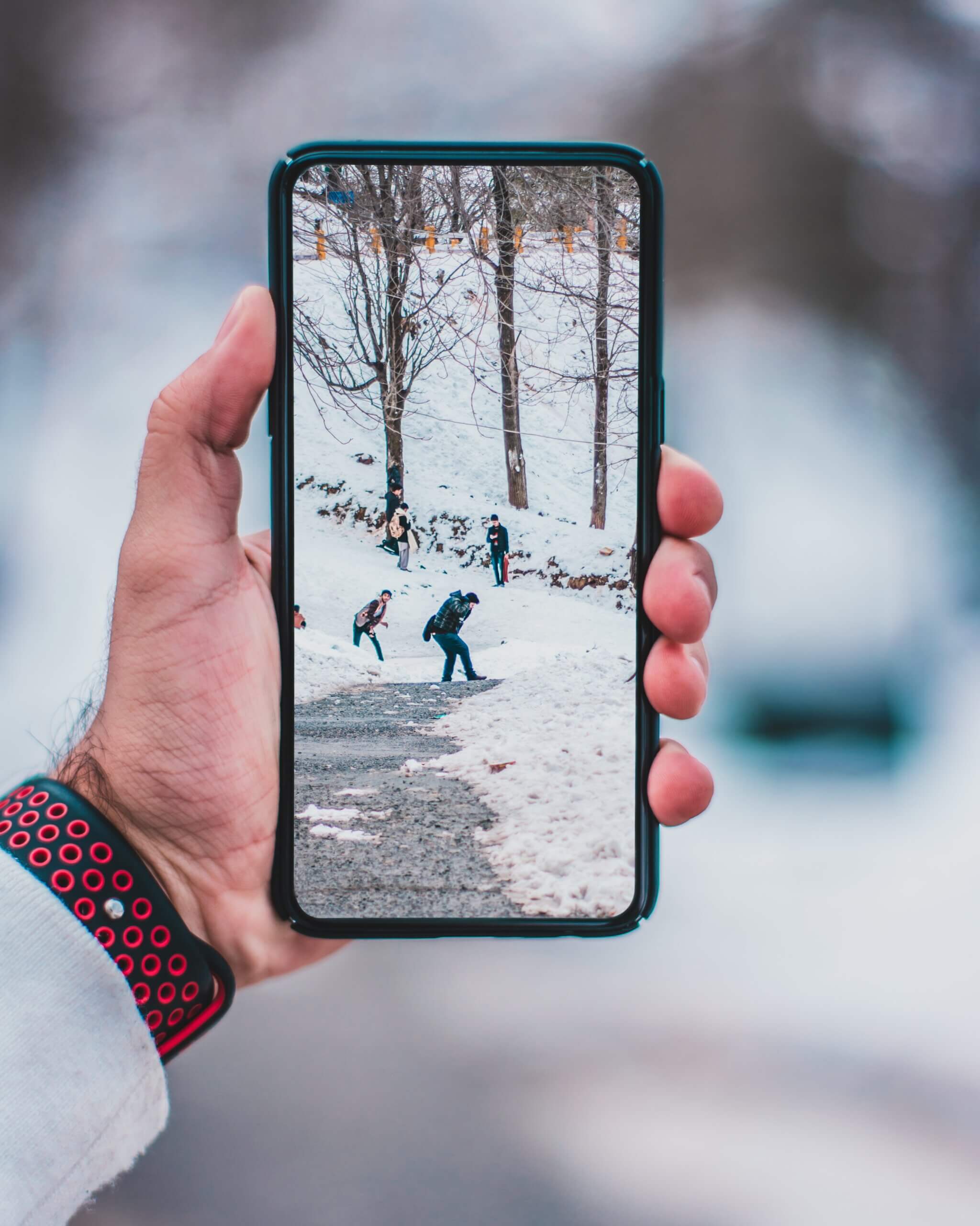 Na fotografii widać telefon z włączonym zdjęciem, przedstawiającym dzieci bawiące się na śniegu.